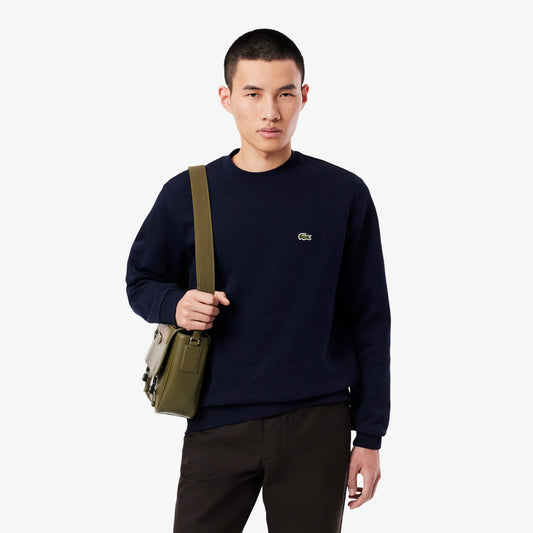 Man wearing a navy blue sweatshirt with a brand logo, holding a green bag on a white background