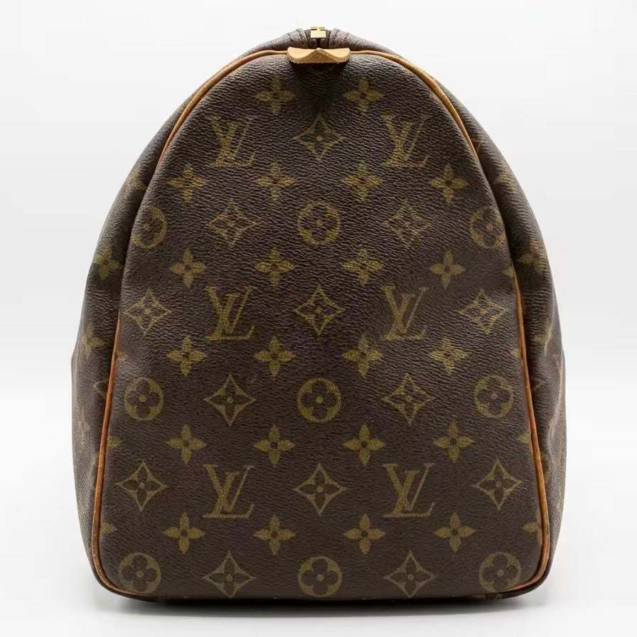 Side profile view of an authentic Louis Vuitton Keepall travel bag in brown monogram canvas, showcasing the iconic rounded silhouette, clean vachetta leather piping, and precise pattern alignment.