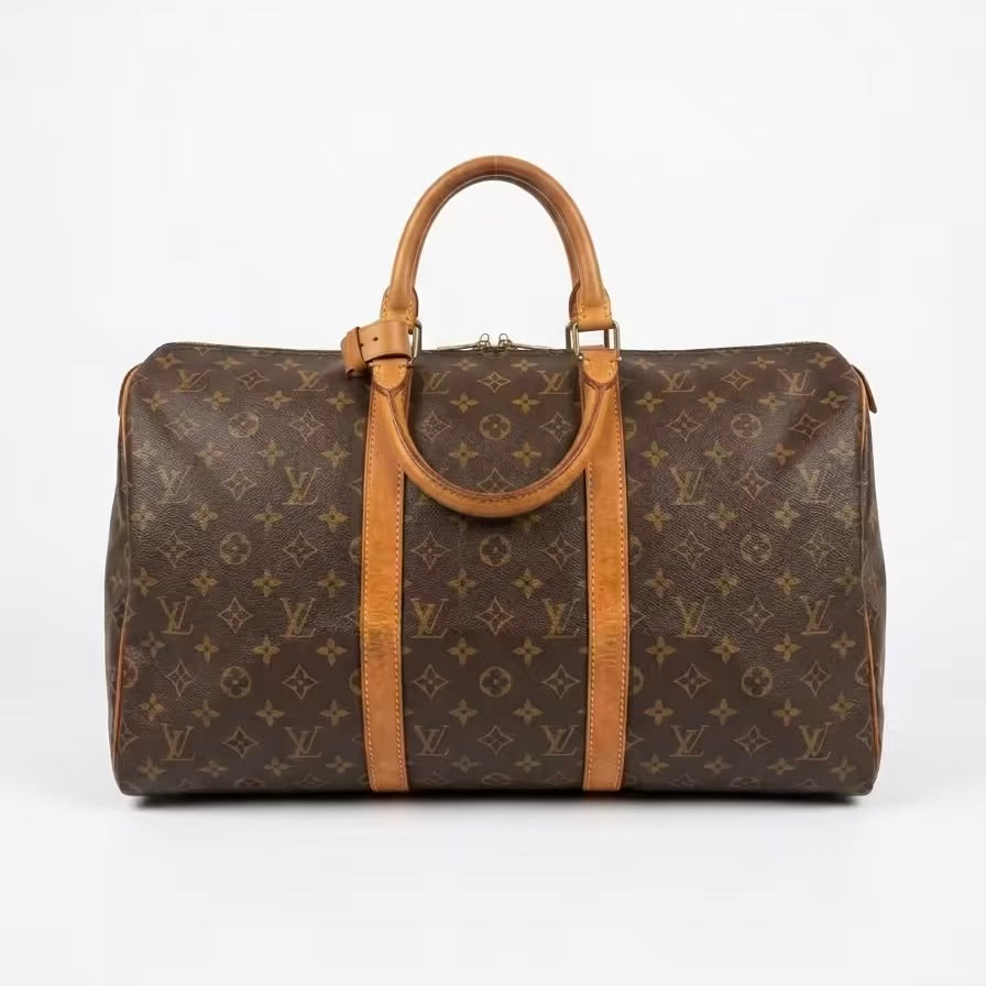 Authentic Louis Vuitton Keepall monogram canvas travel duffle bag featuring dual top leather handles with a matching leather handle keeper, brass hardware, and a rich, golden vachetta patina.