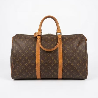 Authentic Louis Vuitton Keepall monogram canvas travel duffle bag featuring dual top leather handles with a matching leather handle keeper, brass hardware, and a rich, golden vachetta patina.