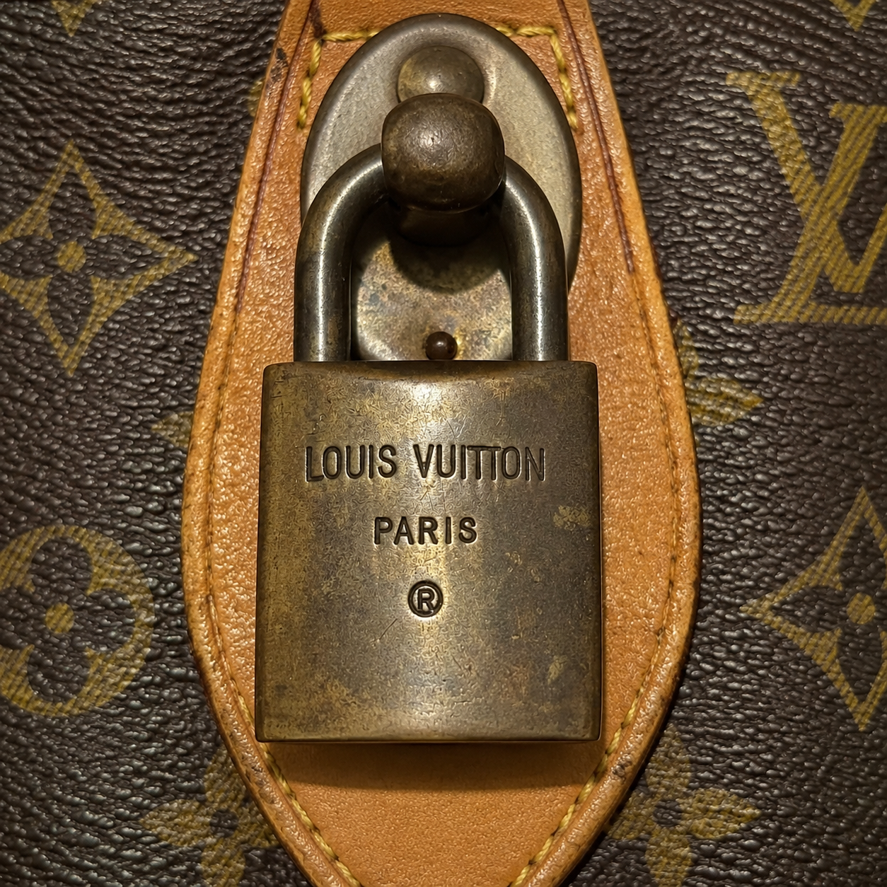 Close-up of an authentic vintage Louis Vuitton brass padlock engraved with the Louis Vuitton Paris registered trademark logo, attached to a monogram canvas Keepall duffle bag.