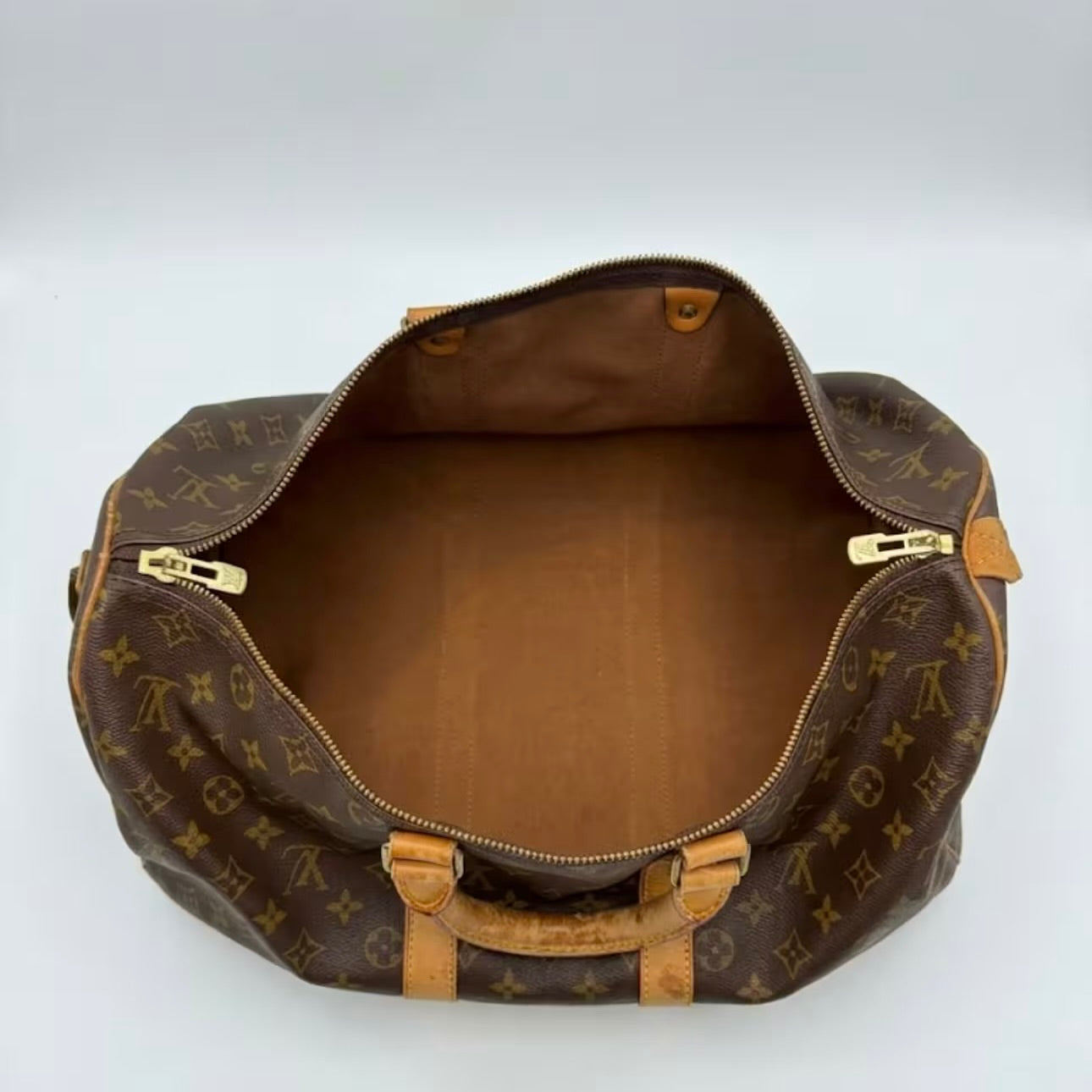 Interior view of an authentic Louis Vuitton Keepall travel duffle bag, showcasing a clean, spacious brown canvas lining and functional double gold-tone zippers.