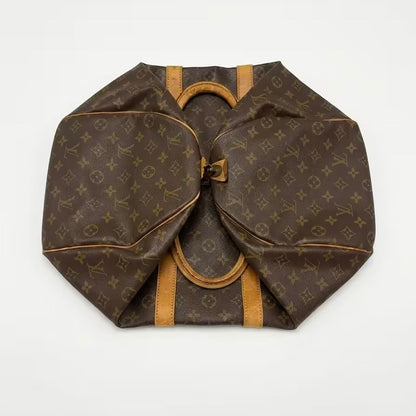 An overhead studio shot of a classic Louis Vuitton monogram canvas travel duffle bag folded completely flat, demonstrating its packable, space-saving design and authentic leather trim layout.⁠