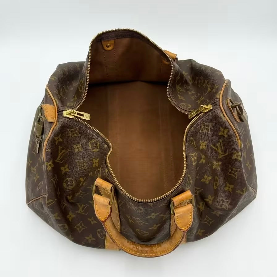 High-angle overhead view of an authentic open Louis Vuitton Keepall monogram travel bag, revealing a clean canvas lining, gold-tone hardware, and the natural vachetta leather top handles.