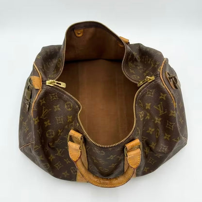 High-angle overhead view of an authentic open Louis Vuitton Keepall monogram travel bag, revealing a clean canvas lining, gold-tone hardware, and the natural vachetta leather top handles.