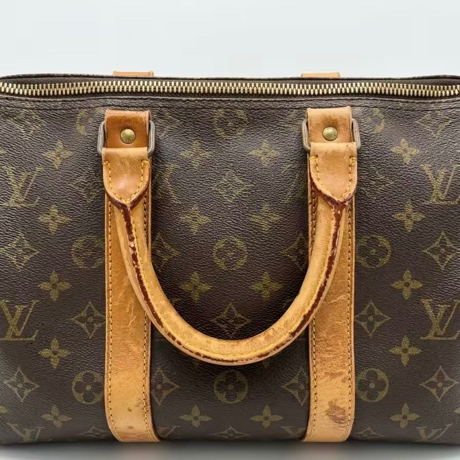 A front-facing view of a vintage Louis Vuitton monogram travel bag, showcasing the iconic canvas pattern, golden top zipper closure, and sturdy vachetta leather handles with a warm, authentic patina.⁠