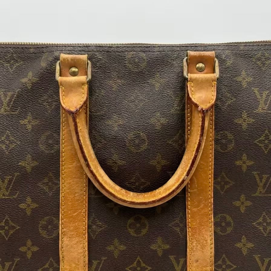 Close-up shot of an authentic Louis Vuitton monogram travel bag's rolled leather top handle, showcasing a rich, honey-toned vintage patina, sturdy contrast stitching, and aged brass rivets.⁠
