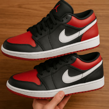 Red, black, and white sneakers with a Nike logo held by a hand on a wooden surface