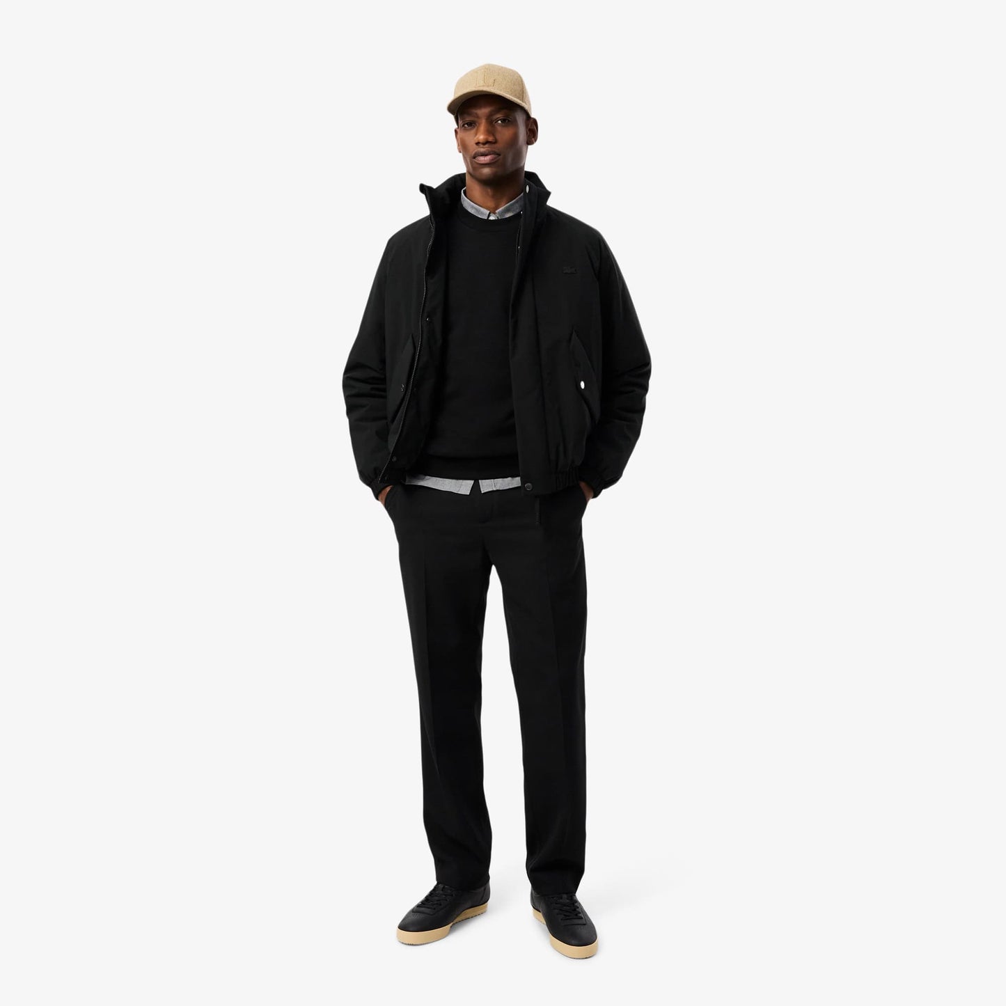 Man wearing a black jacket, black pants, and a beige cap on a white background
