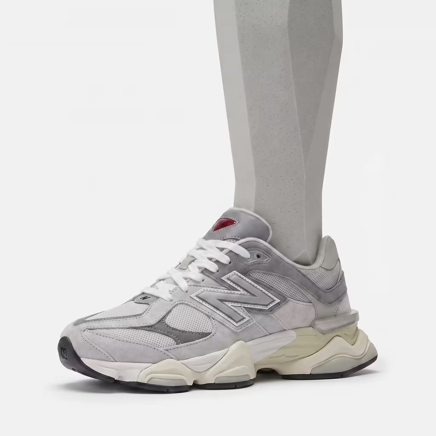 Flat-lay technical view of the outsole of the New Balance 9060 Rain Cloud Grey, showing the clean, unvarnished black and cream rubber pod design with diamond traction patterns, whilst being worn by a geometric  neutral mannequin-style foot.