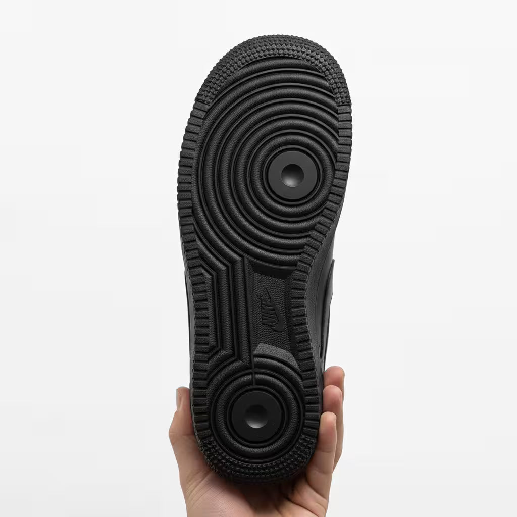 Black sole of a nike air force 1 black sneaker held by a hand on a white background