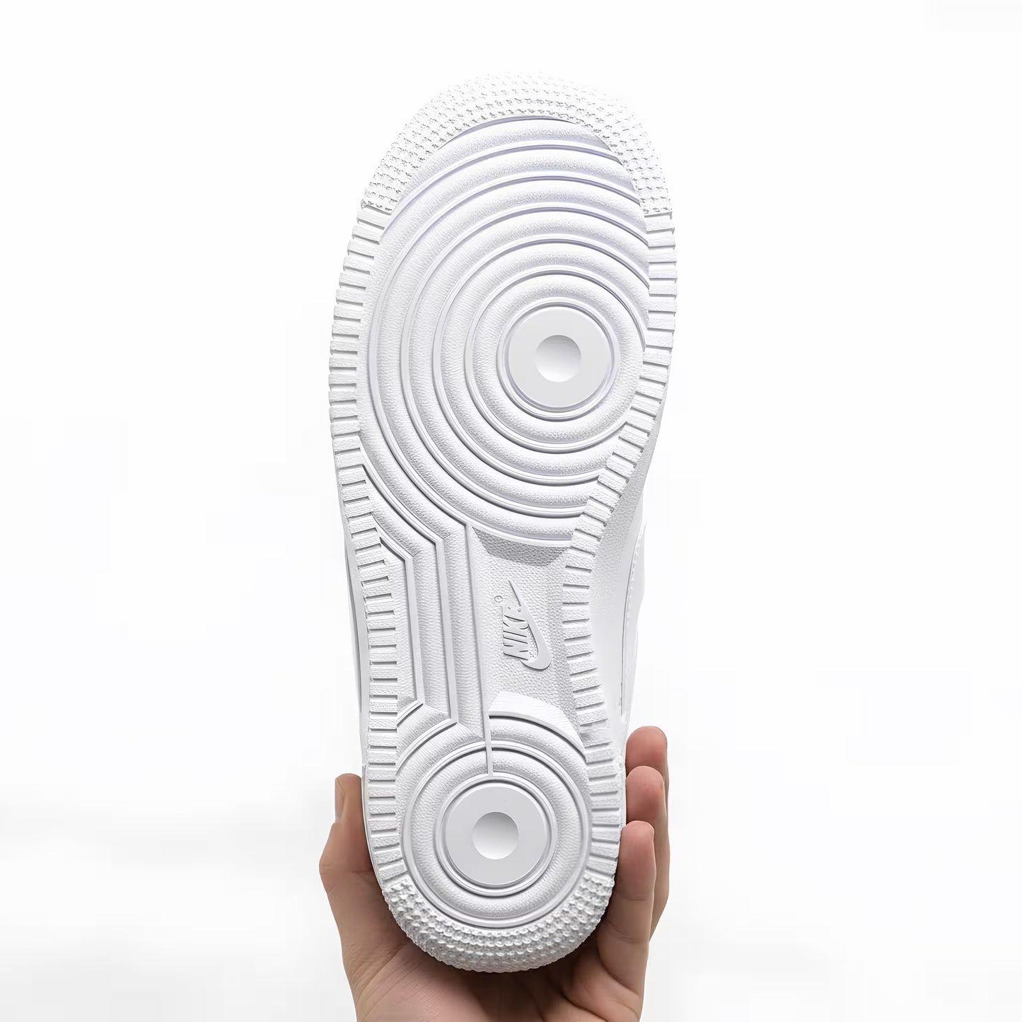 A White Nike Air Force 1 sneaker sole held by a hand on a white background