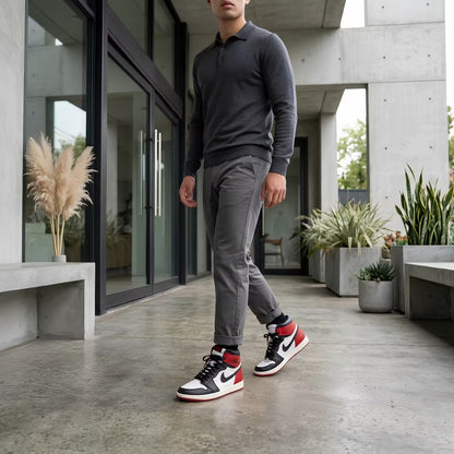 Man wearing a gray sweater and pants with black and red jordan shoes in an outdoor setting.